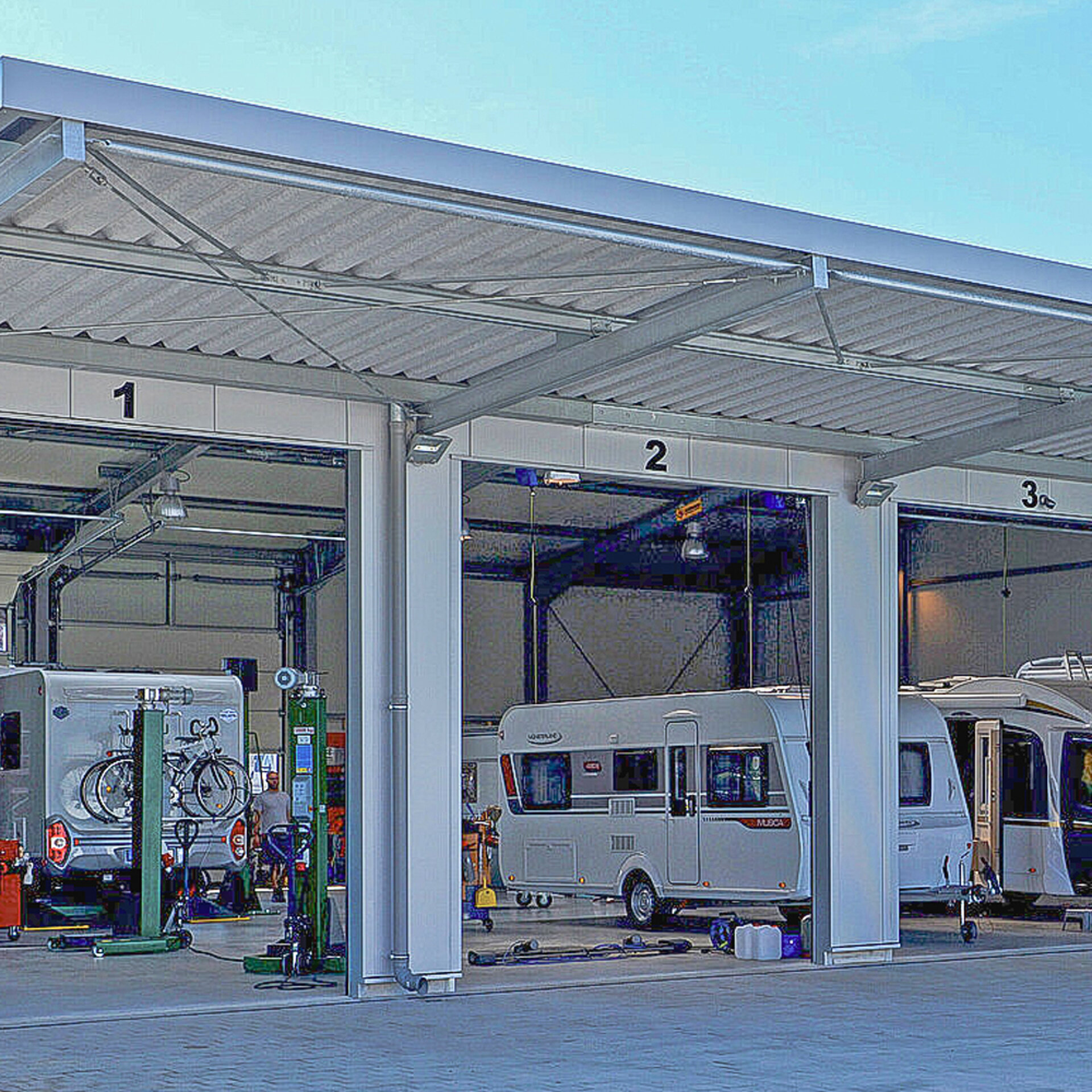 Halle mit Hebebühnen und einem Wohnwagen.