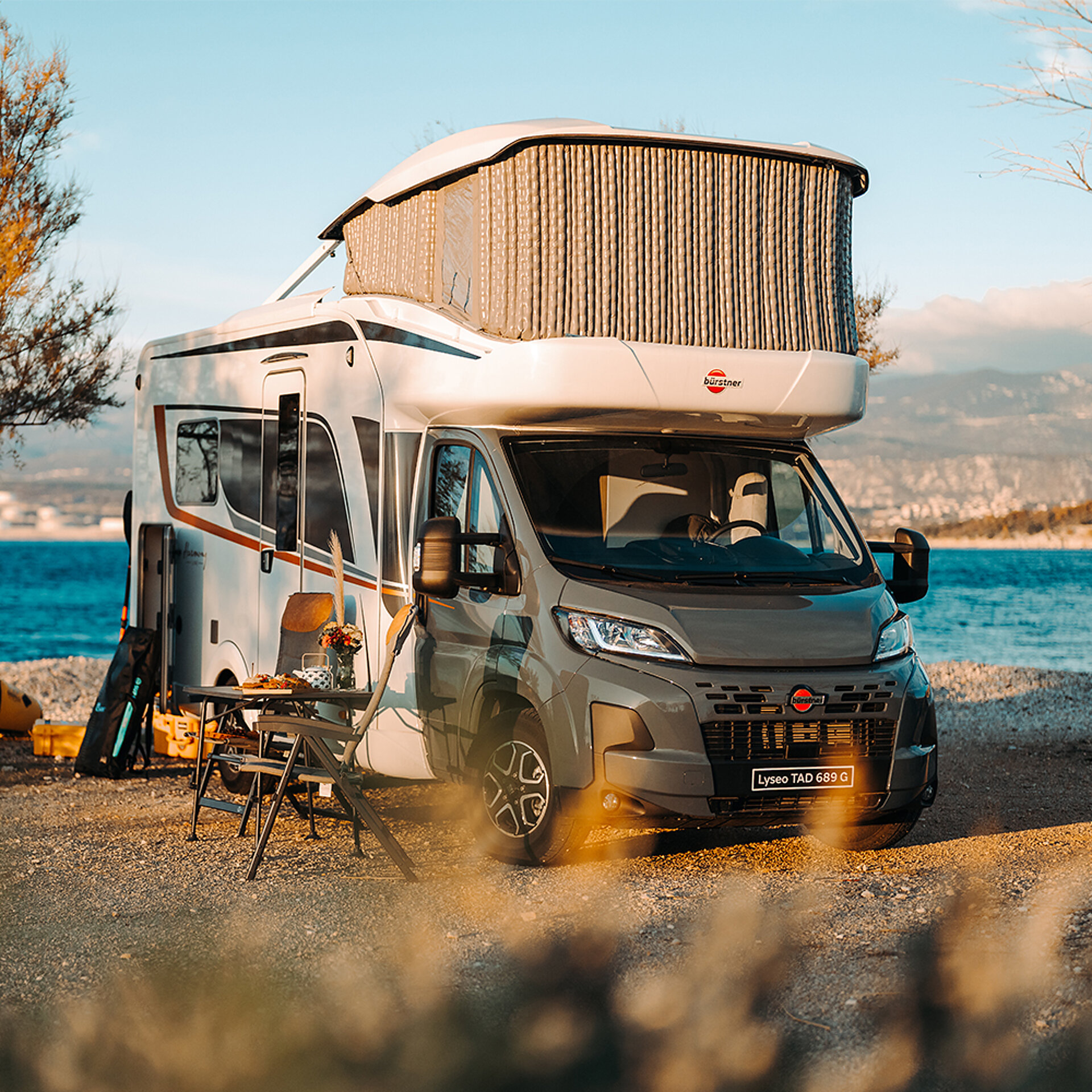 Alkoven-Wohnmobil vor einem See auf einem Stellplatz.